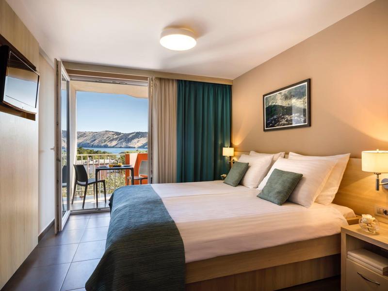 Habitación de hotel acogedora con cama doble, balcón y vista al paisaje en luz diurna.