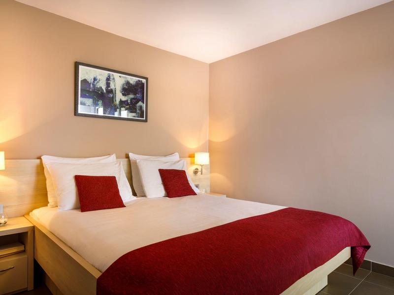 Habitación de hotel acogedora con cama doble, ropa blanca, acentos rojos y dos lámparas de noche.