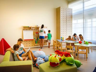 Bambini giocano e disegnano in una stanza giochi colorata e luminosa con giocattoli e ampie finestre.