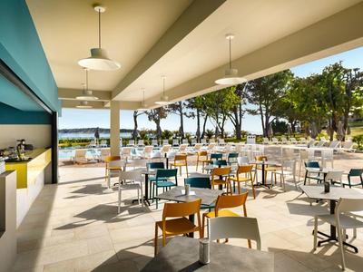 Ristorante all'aperto con sedie colorate e vista su alberi e mare.