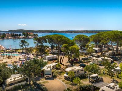 Campingplatz mit Wohnwagen, Bäumen und Blick auf eine Bucht bei klarem Himmel.