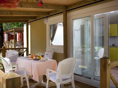 Venkovní jídelní prostor s prostřeným stolem a bílými židlemi vedle posuvných skleněných dveří.