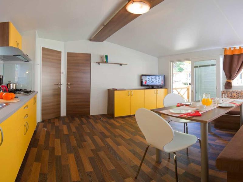 Modern kitchen and dining area with yellow cabinets and wooden flooring in a bright room.