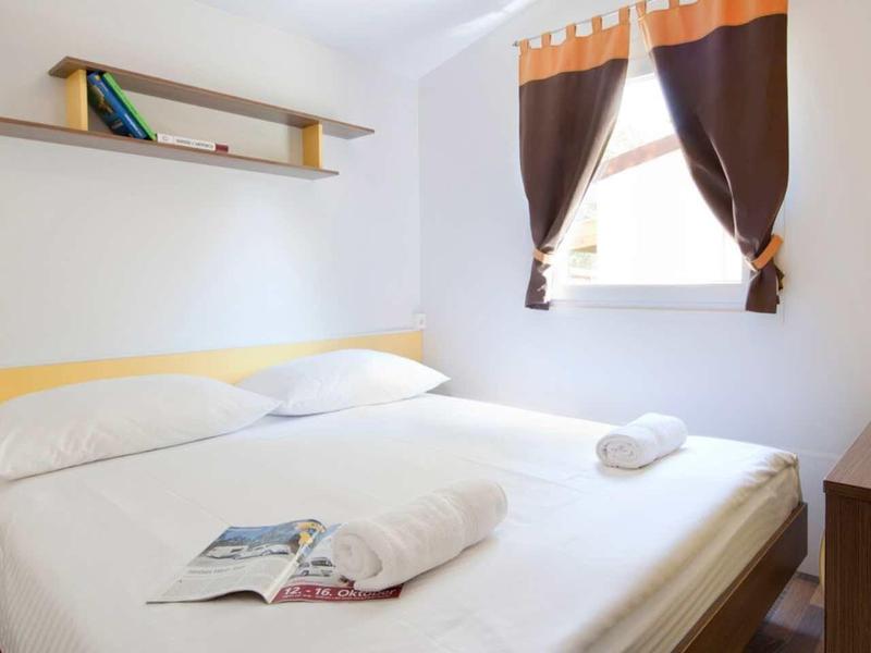 Bright, simple bedroom with double bed, window, and bookshelf.