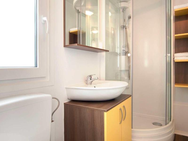 Modern bathroom with glass shower, sink on wooden cabinet, and shelves with towels.