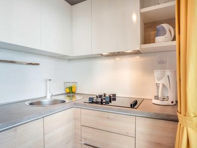 Moderní malý kuchyňský kout s varnou deskou, dřezem, kávovarem a žlutou záclonou.