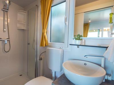 Kleines Badezimmer mit runder Waschschale, Toilette und Duschbereich mit Gelbvorhängen.