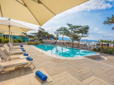 Poolbereich mit Liegestühlen und Sonnenschirmen neben Blick auf das Meer bei klarem Himmel