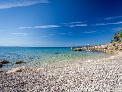 Kamenná pláž s čistou modrou vodou a skalnatým pobřežím pod modrou oblohou.