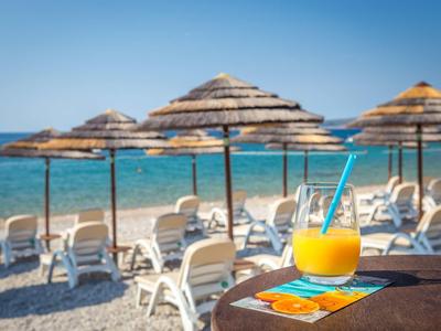 Strand mit Liegestühlen, Strohsonnenschirmen und einem Glas Orangensaft auf einem Tisch.
