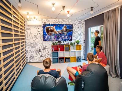 Mladí lidé odpočívají v moderní místnosti s sedacími vaky a velkou televizí.