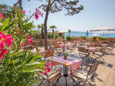 Terrasse eines Hotels mit Tischen und Stühlen, umgeben von Blumen und Blick auf das Meer.