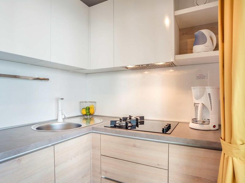 Moderní malý kuchyňský kout s varnou deskou, dřezem, kávovarem a žlutou záclonou.