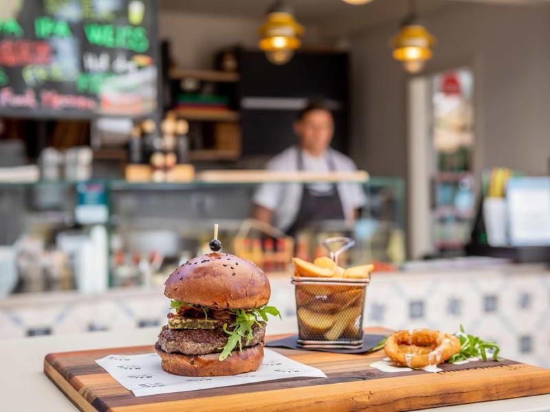 Šťavnatý burger s hranolkami a nápojem na dřevěném prkně v moderní kavárně