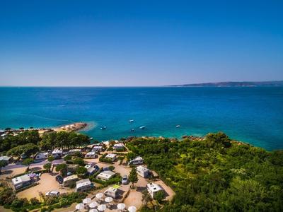 View of a coastal campsite with green vegetation and blue sea in the background.