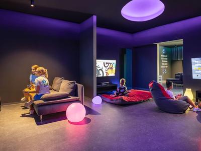 Modern hotel game room with bean bags, TV screens, and colorful lighting.
