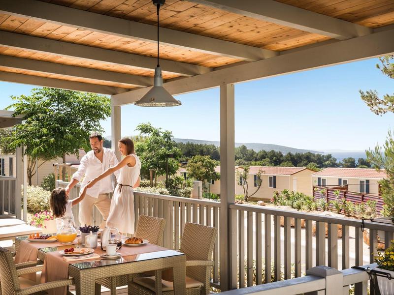 A couple in white robes enjoys the morning on a terrace with breakfast table and scenic view.