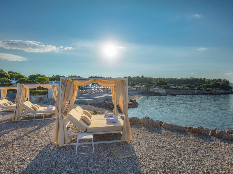 Cozy daybeds with curtains on the rocky beach under a sunny sky.