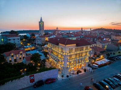 Stadtpanorama bei Sonnenuntergang mit beleuchtetem Gebäude und geparkten Autos in der Straße.