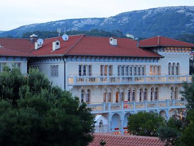 Groot gebouw met rood dak tegen een bebost berglandschap bij schemering.