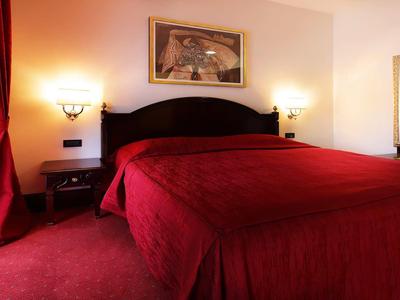 Hotelkamer met groot bed, rode gordijnen en tapijt, warm verlicht.