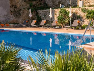 Blauw zwembad met ligstoelen en parasols in een zonnige tuinomgeving.