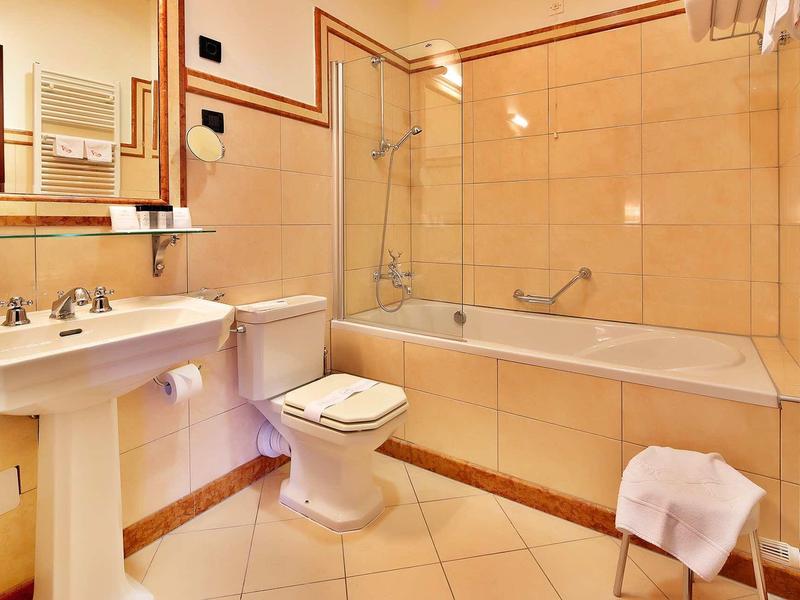 Baño luminoso con espejo grande, bañera, inodoro y lavabo en hotel.