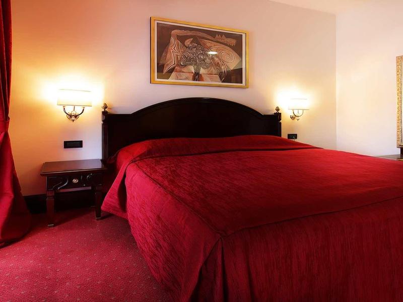 Acogedora habitación de hotel con cama grande, ropa de cama roja y cortinas rojas, iluminada cálidamente.