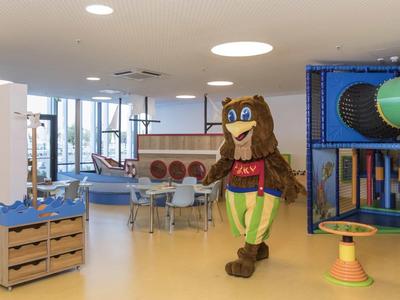 Kolorowy, wewnętrzny plac zabaw dla dzieci z maskotką, siedzeniami i konstrukcją do wspinaczki.