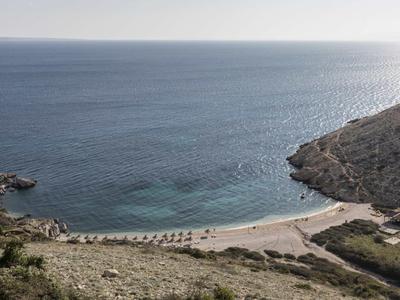 Výhled na klidnou zátoku s čistou vodou a malou písečnou pláží mezi skalnatými kopci.