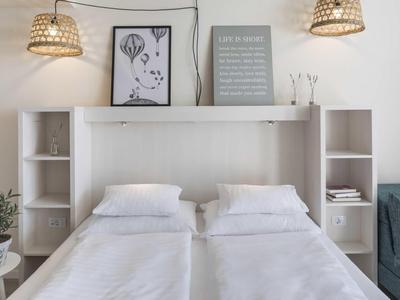 Moderní manželská postel s bílým ložním prádlem, policemi a dekorativními obrázky nad ní