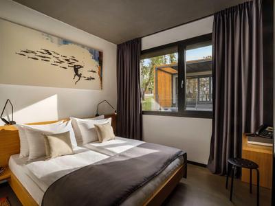 Modern hotel room with double bed, desk, and large window with curtains.