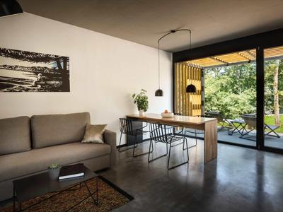 Modern living room with gray sofa, dining table, and view of terrace with green garden.