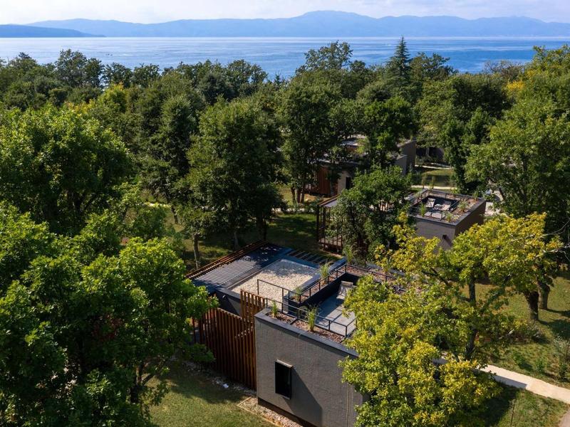 View of a hotel building surrounded by trees overlooking water and mountains in the background.