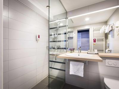 Modern bathroom with washbasin, mirror, glass shower, and towel rack in a hotel room.
