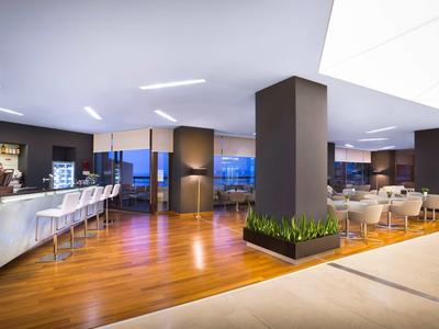 Modern hotel lounge area with bar, wooden floor, and stylish seating under evening light.