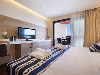 Bright hotel room with double bed, desk, TV, and balcony access with curtains.