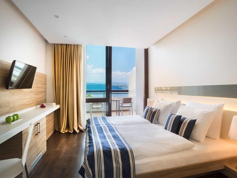 Modern hotel room with bed, TV, sea view, and balcony.