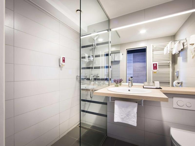 Modern bathroom with washbasin, mirror, glass shower, and towel rack in a hotel room.
