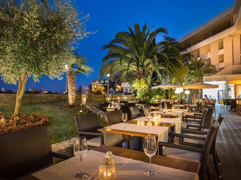 Illuminated hotel terrace with set tables and palm trees at dusk.