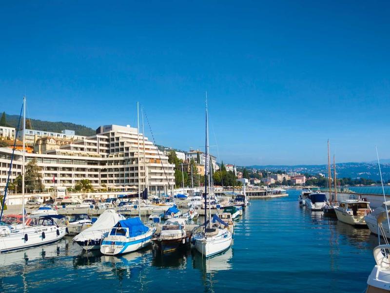 Marina with boats in front of large hotels under clear blue sky.