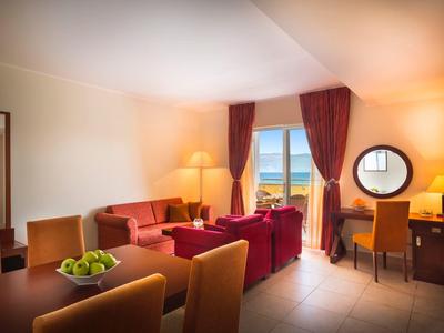 Helles Wohnzimmer mit roten Möbeln, großem Fenster, gemütlicher Beleuchtung und Obstschale auf Tisch.