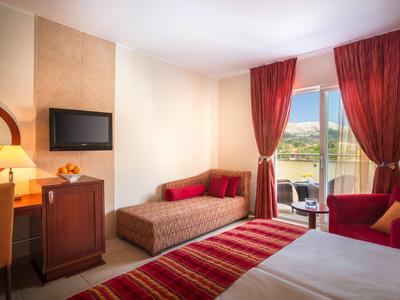 Acogedora habitación de hotel con cama doble, sofá, TV, escritorio y balcón con vistas a la naturaleza.