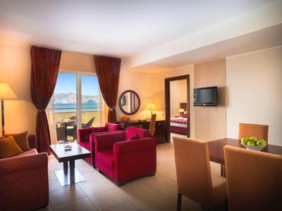 Sala luminosa con sillones rojos, mesa de comedor, TV y balcón con vista a las montañas.