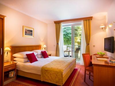 Gemütliches Schlafzimmer mit Doppelbett, roten Kissen, Schreibtisch und Balkon mit grüner Aussicht.