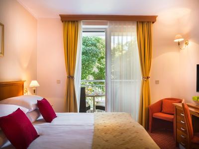 Acogedora habitación de hotel con cama doble, sillón rojo y balcón con vistas a la vegetación.