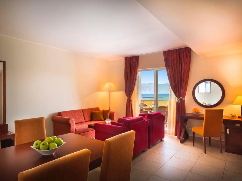 Helles Wohnzimmer mit roten Möbeln, großem Fenster, gemütlicher Beleuchtung und Obstschale auf Tisch.