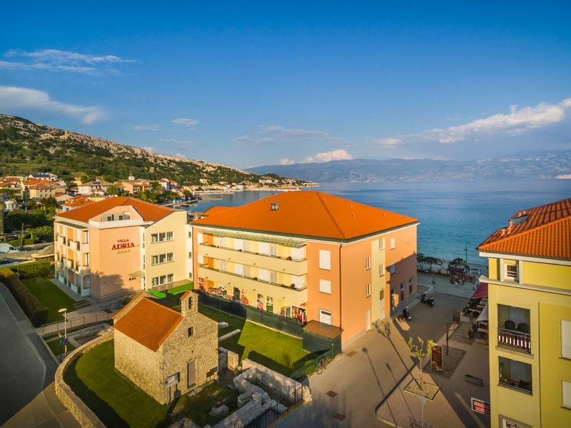 Blick auf orangegedeckte Häuser nahe der Küste mit blauem Himmel und Meer im Hintergrund.