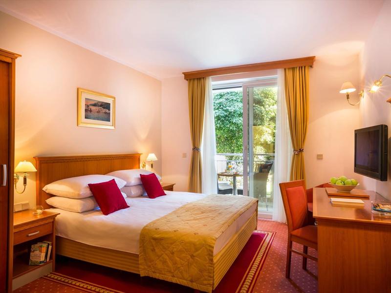 Gemütliches Schlafzimmer mit Doppelbett, roten Kissen, Schreibtisch und Balkon mit grüner Aussicht.