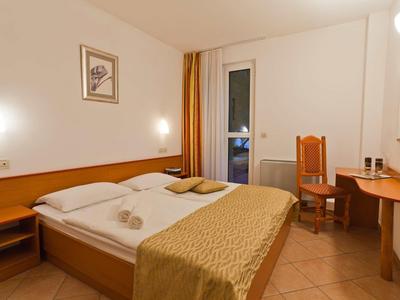 A simply furnished hotel room with double bed, desk, and chair, access to balcony through a door.